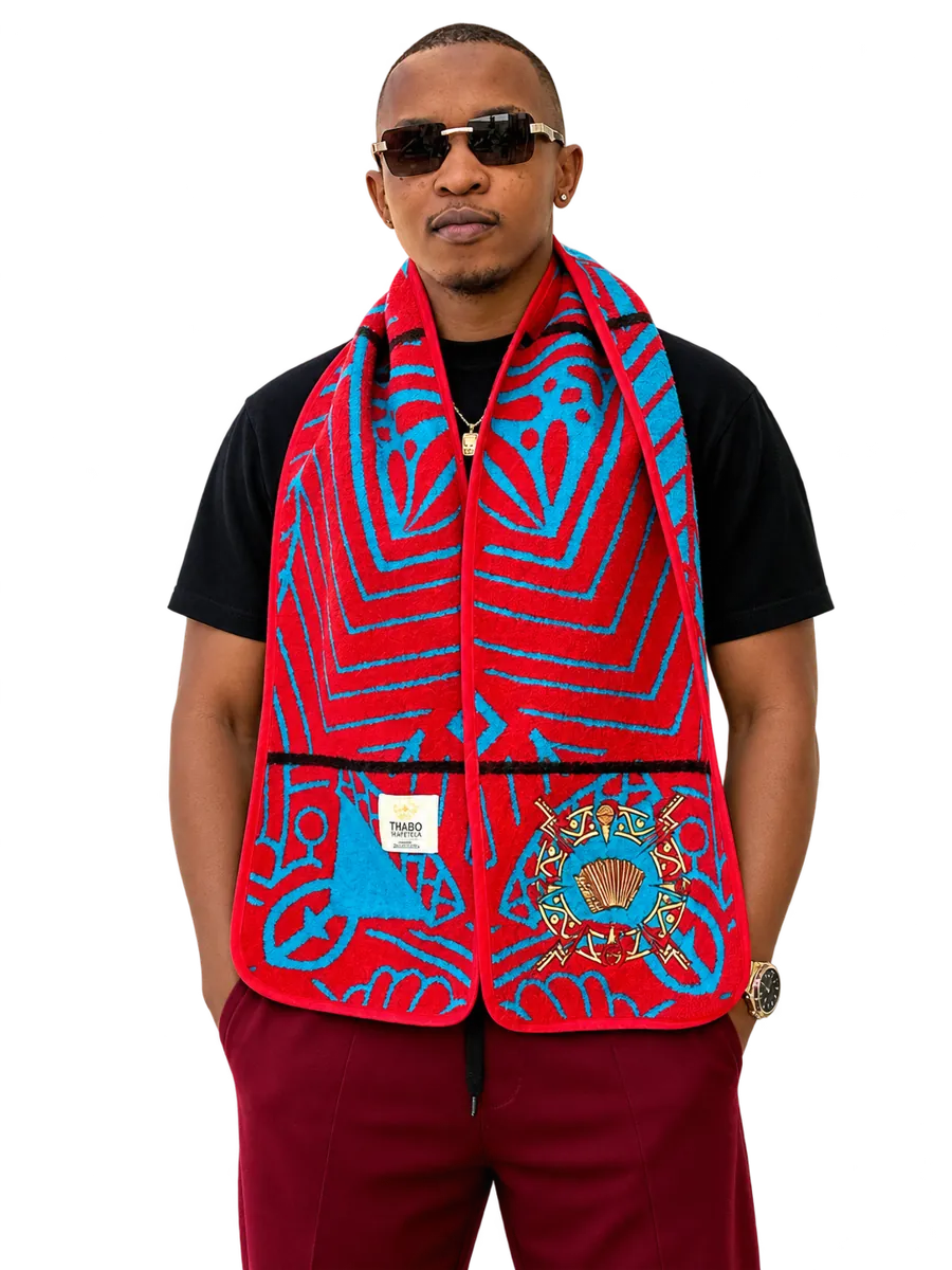 Ntate Stunna in a red and blue Basotho blanket-print scarf over a black tee, maroon trousers and dark shades